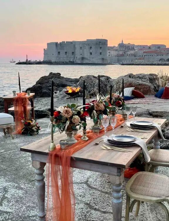 A dinner table set on Banje Beach overlooking Dubrovnik Old Town at sunset